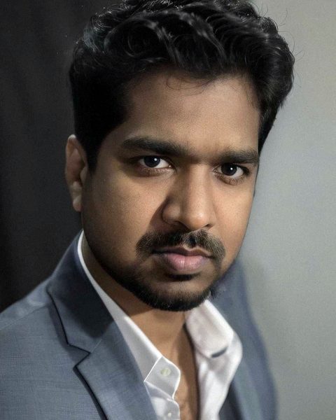 Jithesh Gopinathan, in a grey suit and open-collar white shirt, looking directly at the camera
